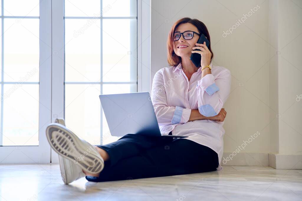 Business woman sitting on the floor with a laptop talking on a smartphone