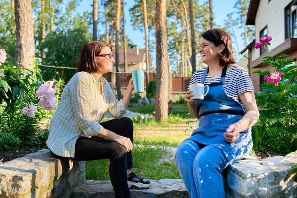 Deux femmes d'âge moyen assises à l'extérieur ensemble dans le jardin, arrière-cour avec des tasses de thé — Photo