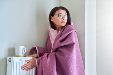 Soğuk kış mevsimi, evde sonbahar mevsimi, ısıtma kaloriferinin yanında donmuş kadın.