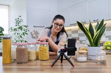 Ev hanımı evde, mutfakta akıllı telefondan video incelemesi yapıyor.
