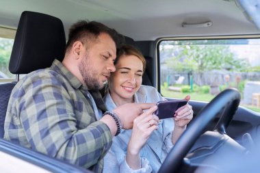 Mutlu orta yaşlı çift arabada birlikte otururken akıllı telefon kullanıyor.