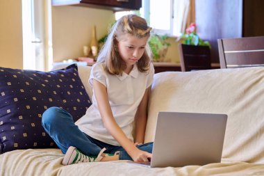 Dizüstü bilgisayarı olan çocuk kanepede oturuyor.