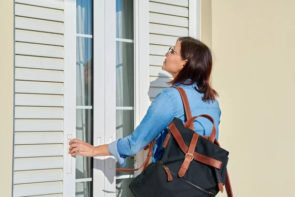 Vrouw met rugzak openen rolluiken buitendeuren op het raam — Stockfoto