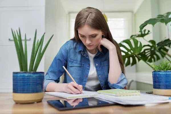 Studente universitaria femminile studia a casa, scrive in un quaderno — Foto Stock