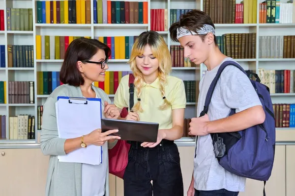 Grupo de estudantes adolescentes e um professor conversando na biblioteca — Fotografia de Stock