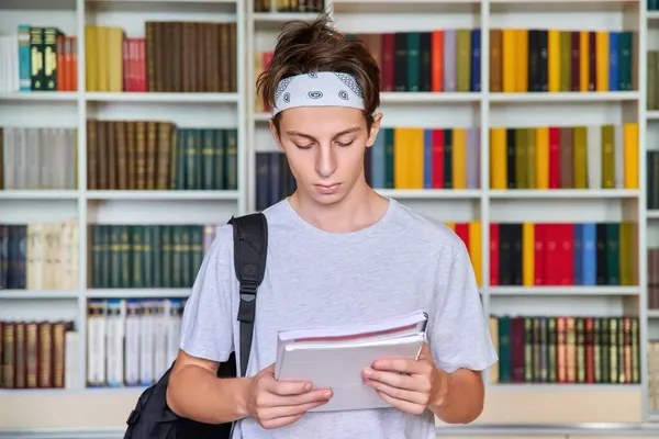 Porträt eines männlichen Teeniestudenten, der in einem Notizbuch in einer Bibliothek sucht. — Stockfoto