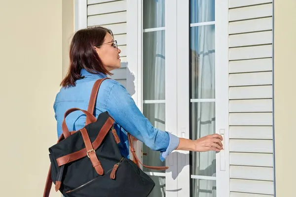 Nő hátizsák nyíló redőnyök kívül ajtók az ablakon — Stock Fotó