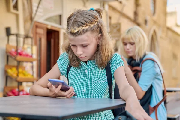 Preadolescente colegiala y estudiante adolescente con mochilas utilizando teléfonos inteligentes, al aire libre —  Fotos de Stock