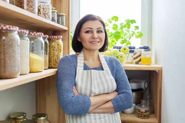 Portrait d'une femme souriante dans un tablier dans la cuisine dans le garde-manger. — Photo