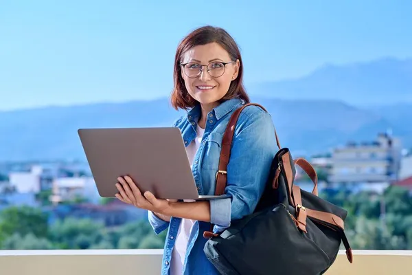 Портрет женщины средних лет в наушниках с ноутбуком и рюкзаком. — стоковое фото