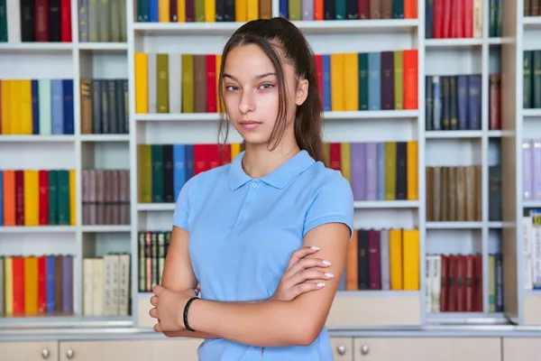 Porträt einer selbstbewussten Schülerin, die in der Bibliothek in die Kamera blickt. — Stockfoto