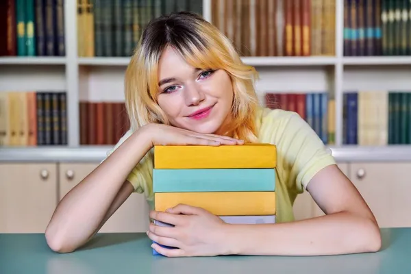 Mujer adolescente estudiante de secundaria mirando a la cámara con libros en la biblioteca —  Fotos de Stock