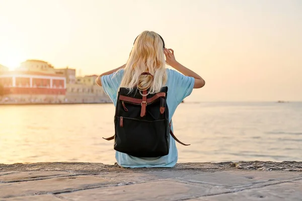 Feliz adolescente hembra en auriculares con mochila disfrutando de la ciudad turística europea, paisaje marino — Foto de Stock