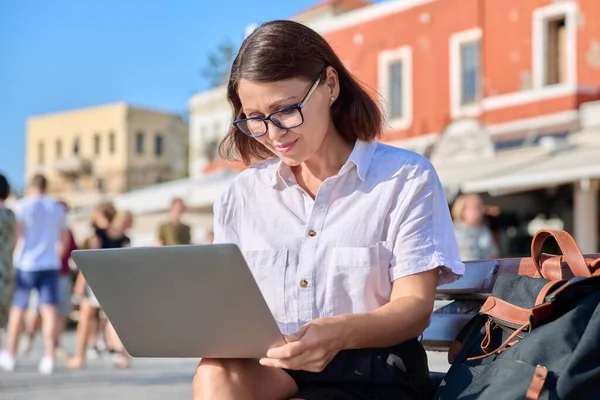 Женщина средних лет сидит на скамейке в городе, используя ноутбук — стоковое фото