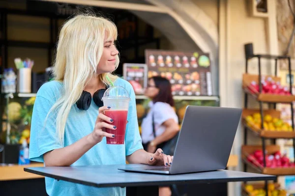 Adolescente em frutas ao ar livre suco de frutas bar beber vitamina suco fresco, usando laptop — Fotografia de Stock