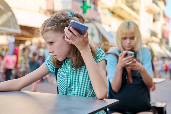 Niñas, niños y adolescentes usando teléfonos inteligentes sentados al aire libre en la ciudad —  Fotos de Stock