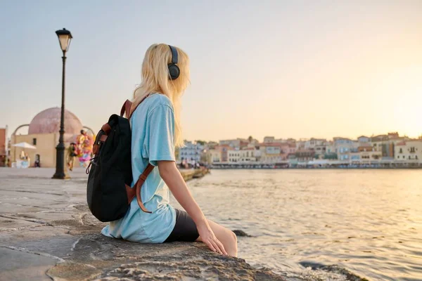 Feliz adolescente hembra en auriculares con mochila disfrutando de la ciudad turística europea, paisaje marino — Foto de Stock