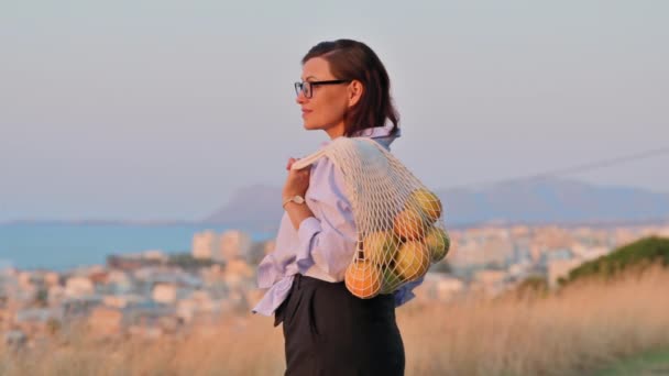 Donna di mezza età con borsa di arance fresche godendo la natura, tramonto, paesaggio marino — Video Stock