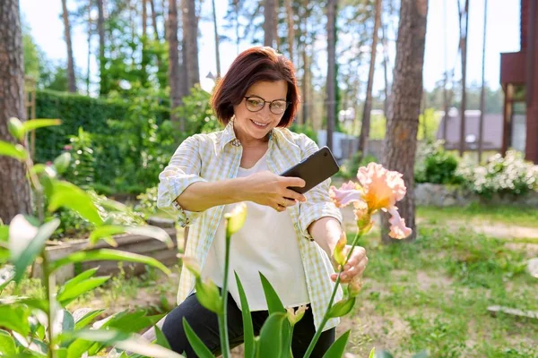 Vrouw in de lente tuin genieten van schoonheid van iris bloemen het nemen van foto 's van iris met smartphone — Stockfoto