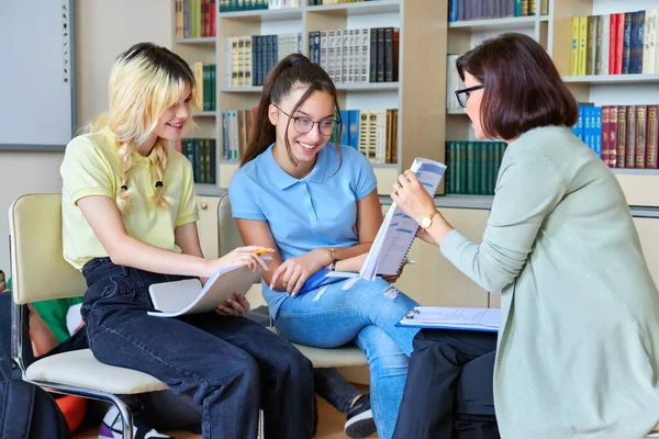 Vrouwelijke leraar werkt met tienerstudenten in de bibliotheek. — Stockfoto