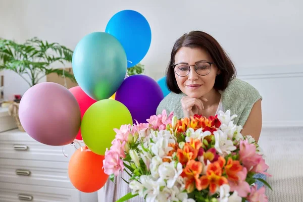 Portret van een vrolijke vrouw van middelbare leeftijd met boeket bloemen, ballonnen — Stockfoto