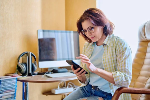 Donna di mezza età che utilizza smartphone seduto in poltrona in ufficio — Foto Stock