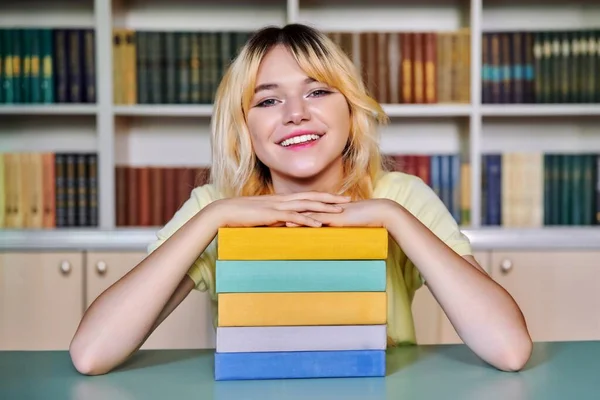 Mujer adolescente estudiante de secundaria mirando a la cámara con libros en la biblioteca —  Fotos de Stock