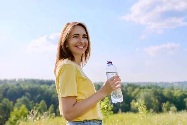 炎炎夏日，女人拿着一瓶水看着镜头，看着我们的自然 — 图库照片