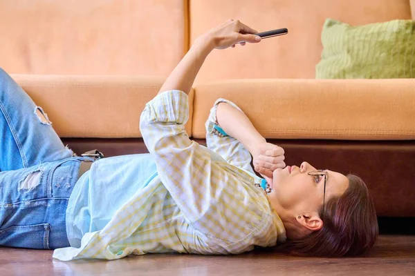 Mujer madura relajándose en casa usando smartphone —  Fotos de Stock