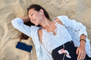 Kulaklıklı, akıllı telefonlu, kumsalda genç bir kadını rahatlatmak.