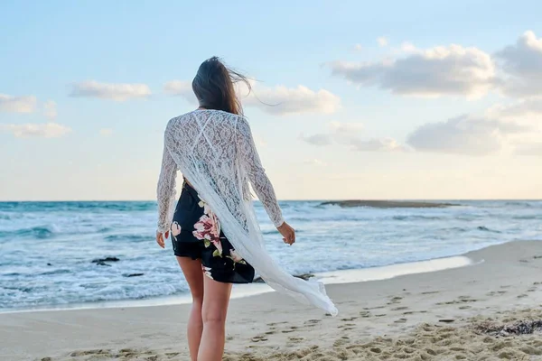 Visão traseira da jovem mulher na moda roupas românticas andando ao longo da praia — Fotografia de Stock