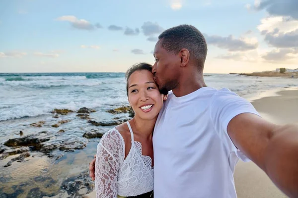 Pareja feliz en el amor besándose tomando selfie juntos en el teléfono inteligente, en la playa — Foto de Stock