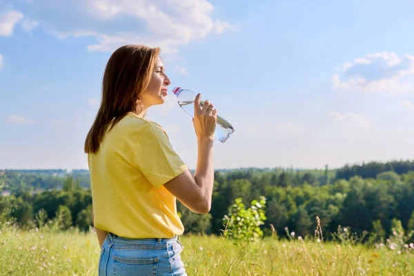 Verano soleado caliente, mujer adulta sedienta que bebe el agua de la botella a nosotros en naturaleza — Foto de Stock
