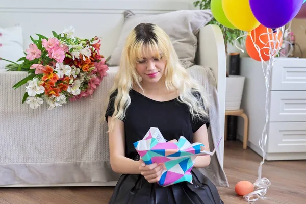 Счастливая девочка-подросток с воздушными шарами и цветами распаковывает подарок — стоковое фото
