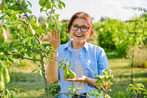 Portret van een glimlachende zelfverzekerde vrouw van middelbare leeftijd in boomgaard, in de buurt van perenboom — Stockfoto