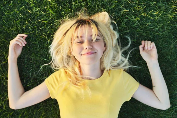 Ovanifrån av en vacker tonåring blond liggande på det gröna gräset. — Stockfoto
