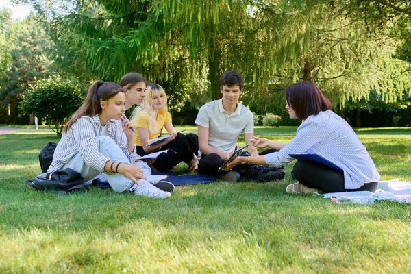 Εξωτερική, ομάδα μαθητών με γυναίκα δασκάλα κάθεται στο γρασίδι — Φωτογραφία Αρχείου