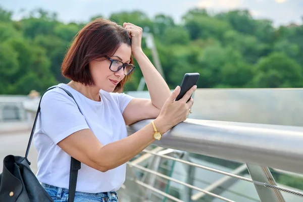 Middle-aged woman using smartphone, walking in the summer city — Stock Photo, Image