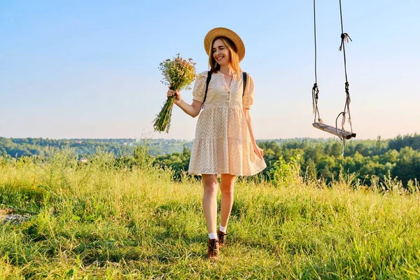Šťastná usměvavá dospělá žena v šatech s kloboukem s kyticí divokých květin. — Stock fotografie