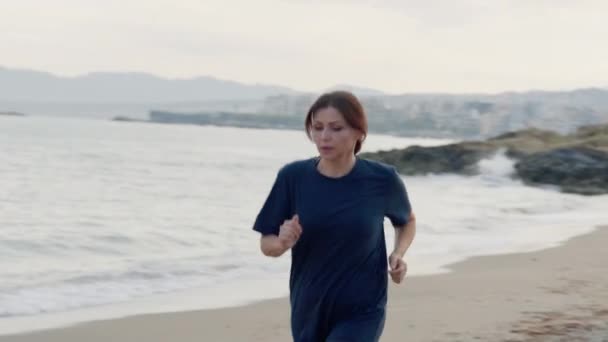 Vera donna di mezza età che corre lungo la spiaggia al mattino. — Video Stock