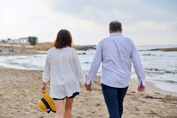 快乐的中年夫妇一起在海滩上散步，回头看 — 图库照片