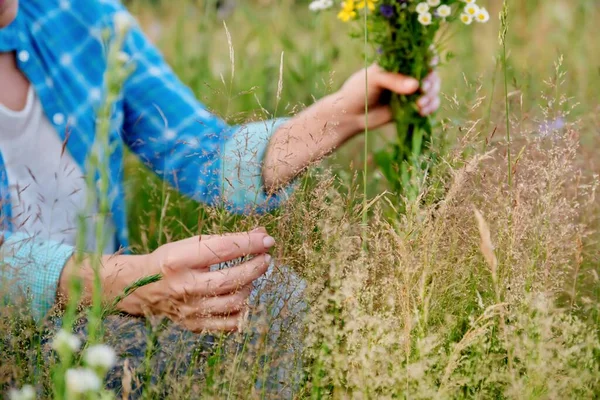 Femme avec bouquet d'herbes de champ et de fleurs touchant les plantes en fleurs dans le champ d'été — Photo