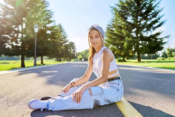 Fashionabla tonårstjej poserar sittande på vägen i parken. — Stockfoto