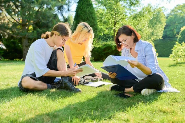 Profesora de escuela, psicóloga, trabajadora social hablando con adolescentes, sentada en la hierba — Foto de Stock