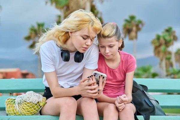 Dos hermanas niñas, adolescentes y preadolescentes miran un teléfono inteligente —  Fotos de Stock