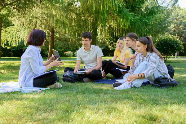 Открытая группа студентов с учительницей, сидящей на траве — стоковое фото