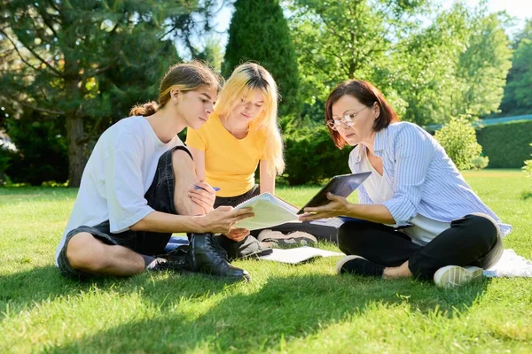Profesora de escuela, psicóloga, trabajadora social hablando con adolescentes, sentada en la hierba — Foto de Stock