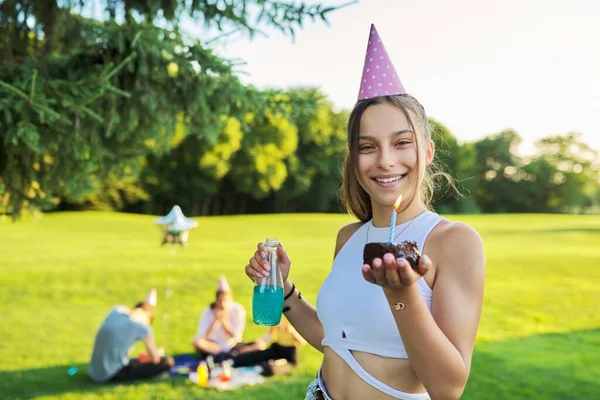 Születésnap, tizenéves lány ünnepi kalapban tortával és gyertyával a szabadban party — Stock Fotó