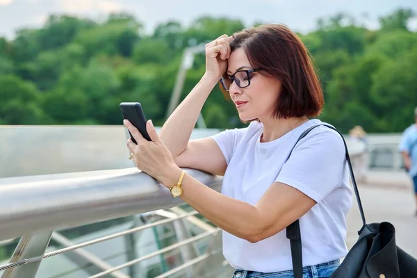 Middle-aged woman using smartphone, walking in the summer city — Stock Photo, Image