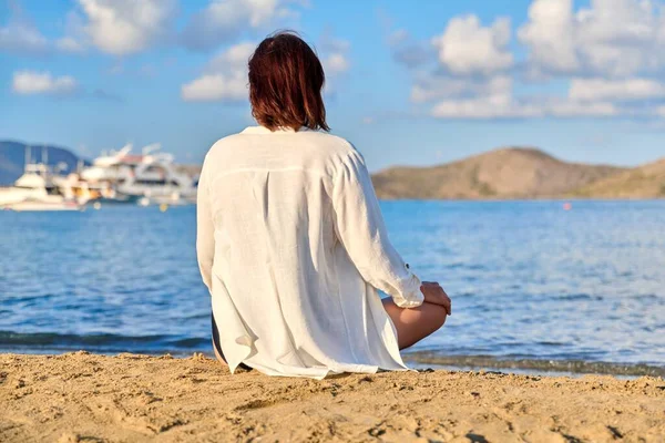 Mature woman sitting in lotus position meditating on the beach, back view — Foto de Stock